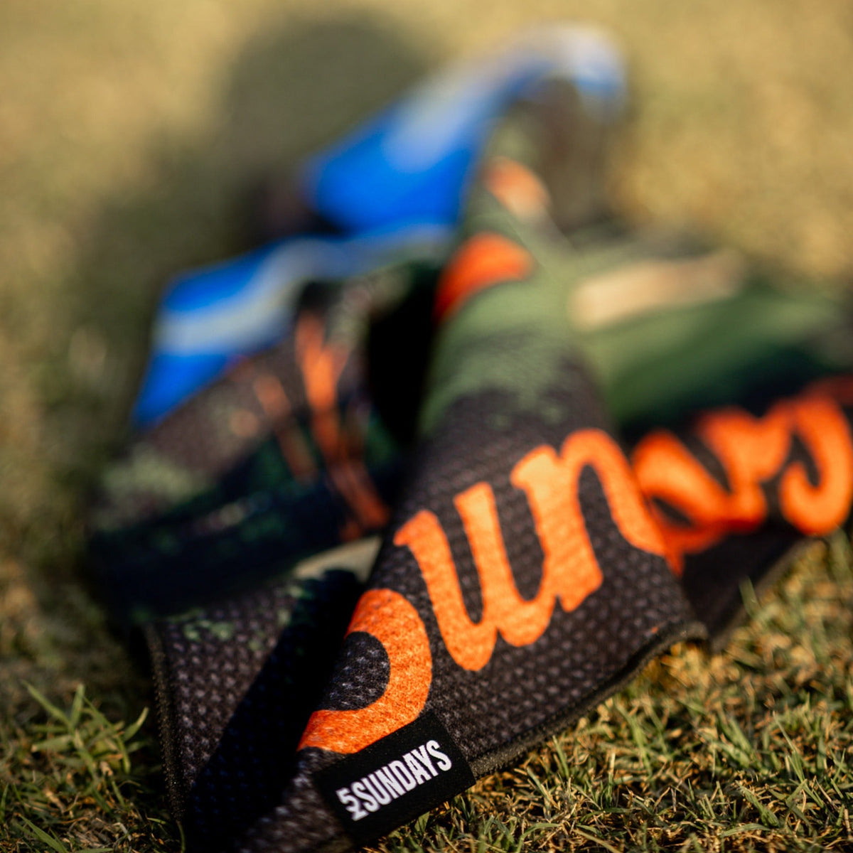Close-up of 52 Sundays golf towels in a golf course pattern print with orange script lettering, laid on grass.