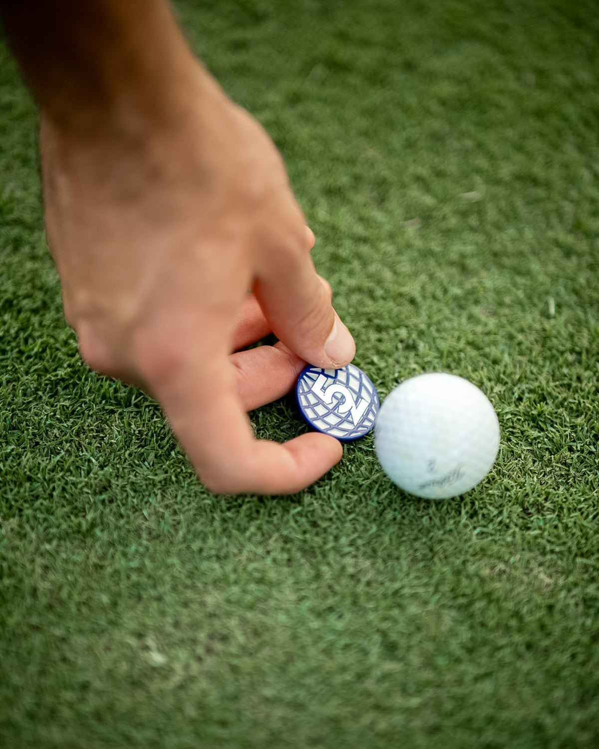 Golfer's hand placing a 52 Sundays globe ball marker on the green next to a golf ball