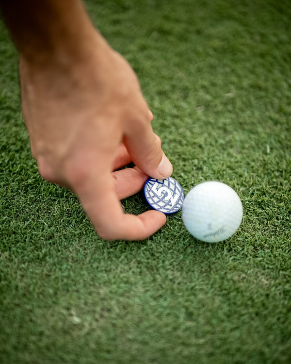 Golfer's hand placing a 52 Sundays globe ball marker on the green next to a golf ball