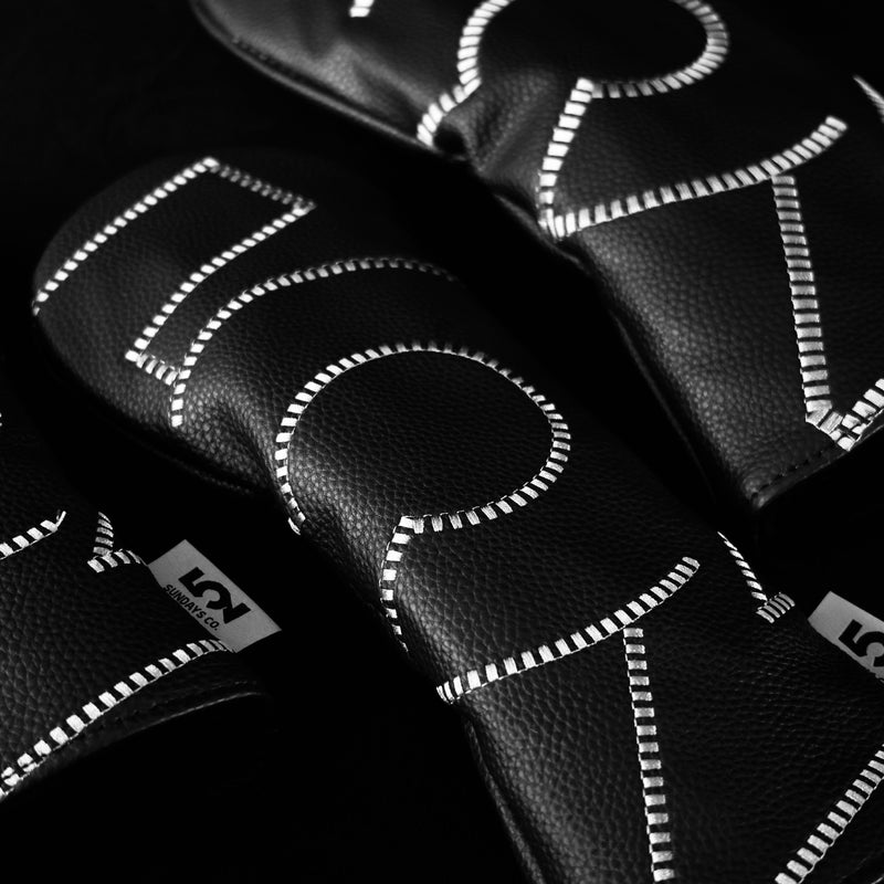 Close-up of black golf club heads with white stitching on a black background