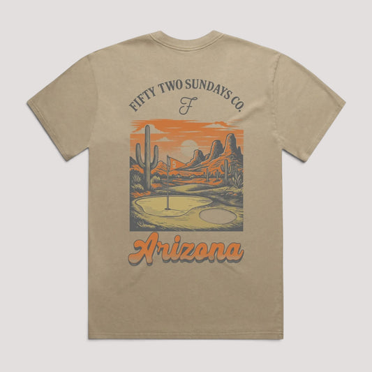 A beige short-sleeve t-shirt with a graphic print on the front. The graphic features a desert landscape with cacti and mountains under an orange sky, with the text 'FIFTY TWO SUNDAYS CO' above and 'Arizona' below.