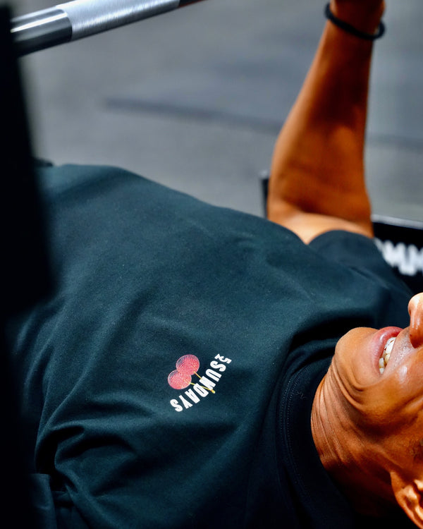 Close-up of the small front "52SUNDAYS" cherries logo on the Sunday Cherries Tee, worn during a bench press.