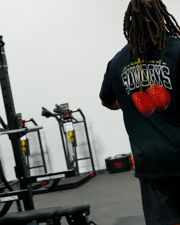 Back view of the Sunday Cherries Tee walking through a gym, cherries graphic visible.