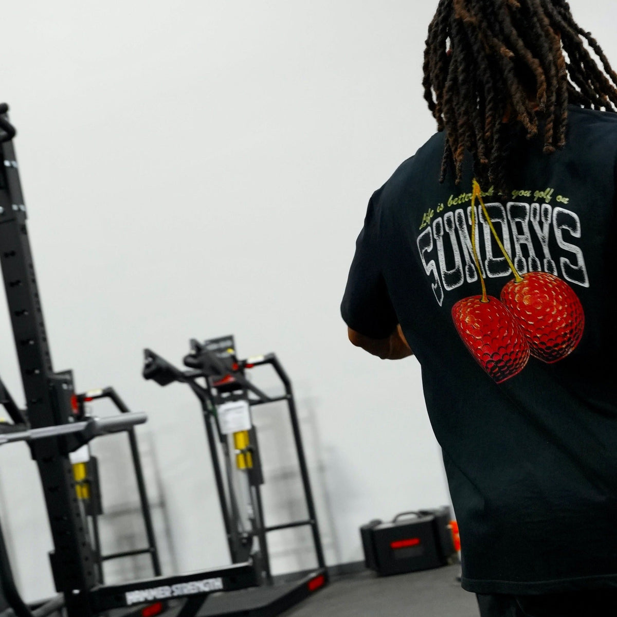 Back view of the Sunday Cherries Tee walking through a gym, cherries graphic visible.