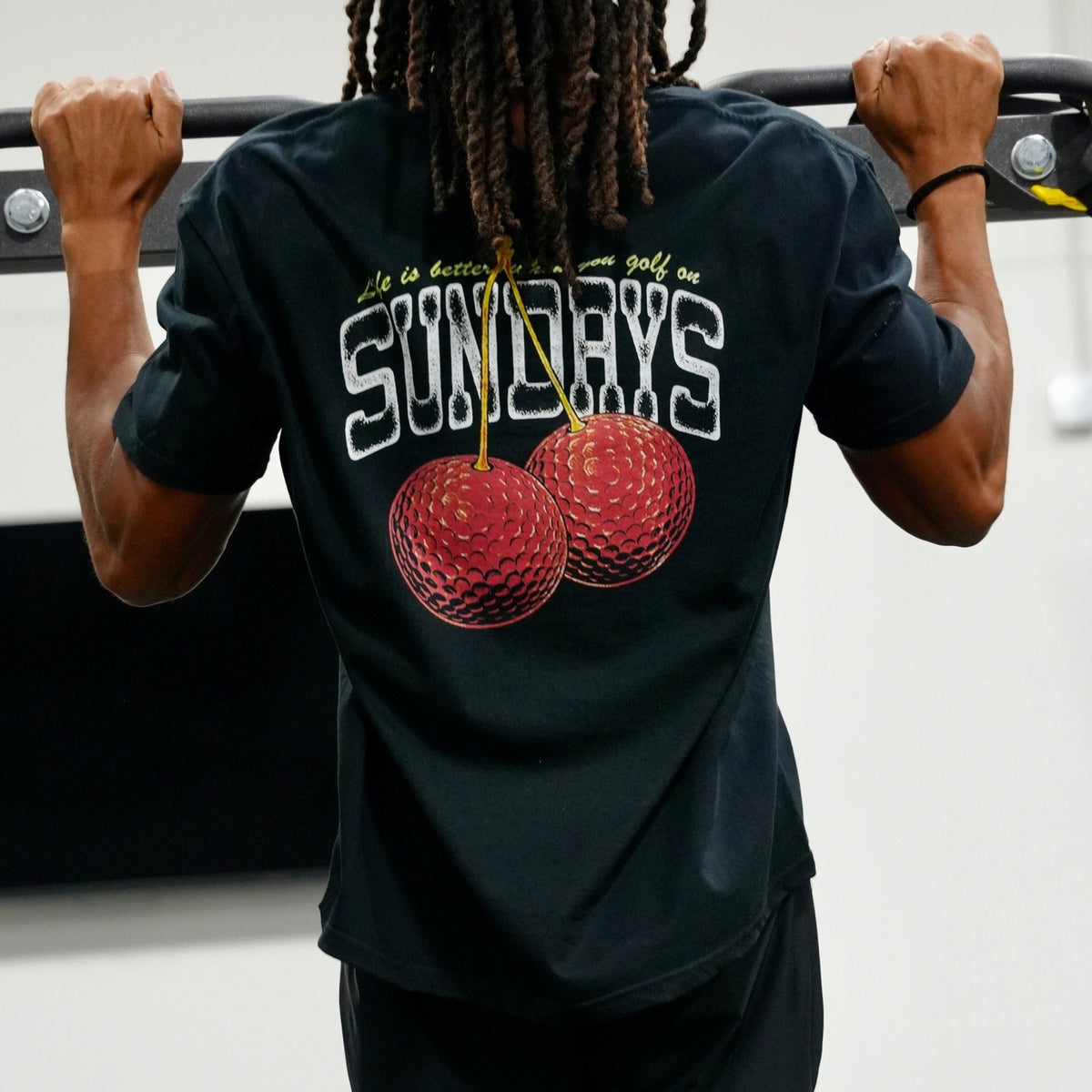 Back view of the Sunday Cherries Tee's full graphic during a pull-up, showing the cherries design and script text.