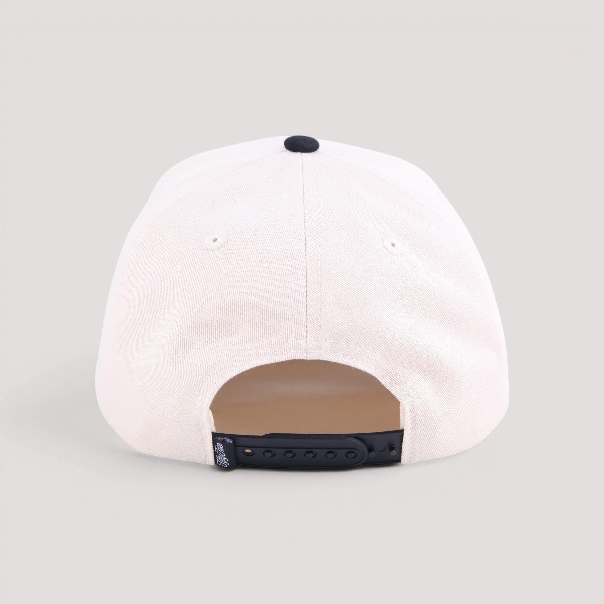 The back view of an off-white baseball cap with a black snapback closure and a black top button, shown on a light gray background.