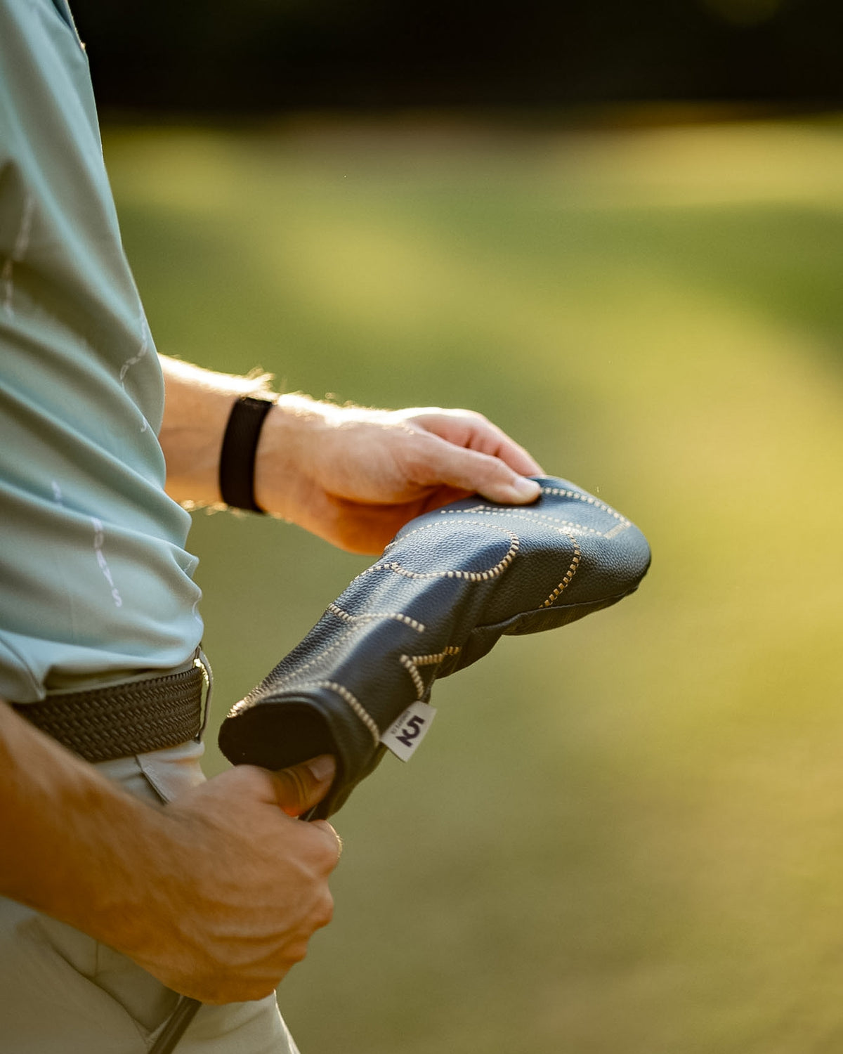 Golfer holding a 52 Sundays navy leather fairway wood headcover in warm evening light, showing the cream stitch detailing and '52' tag