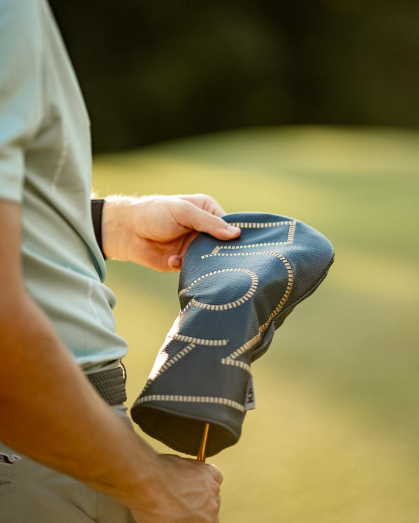 Golfer pulling a 52 Sundays leather headcover off a club in warm evening light, showing the cream stitch detailing