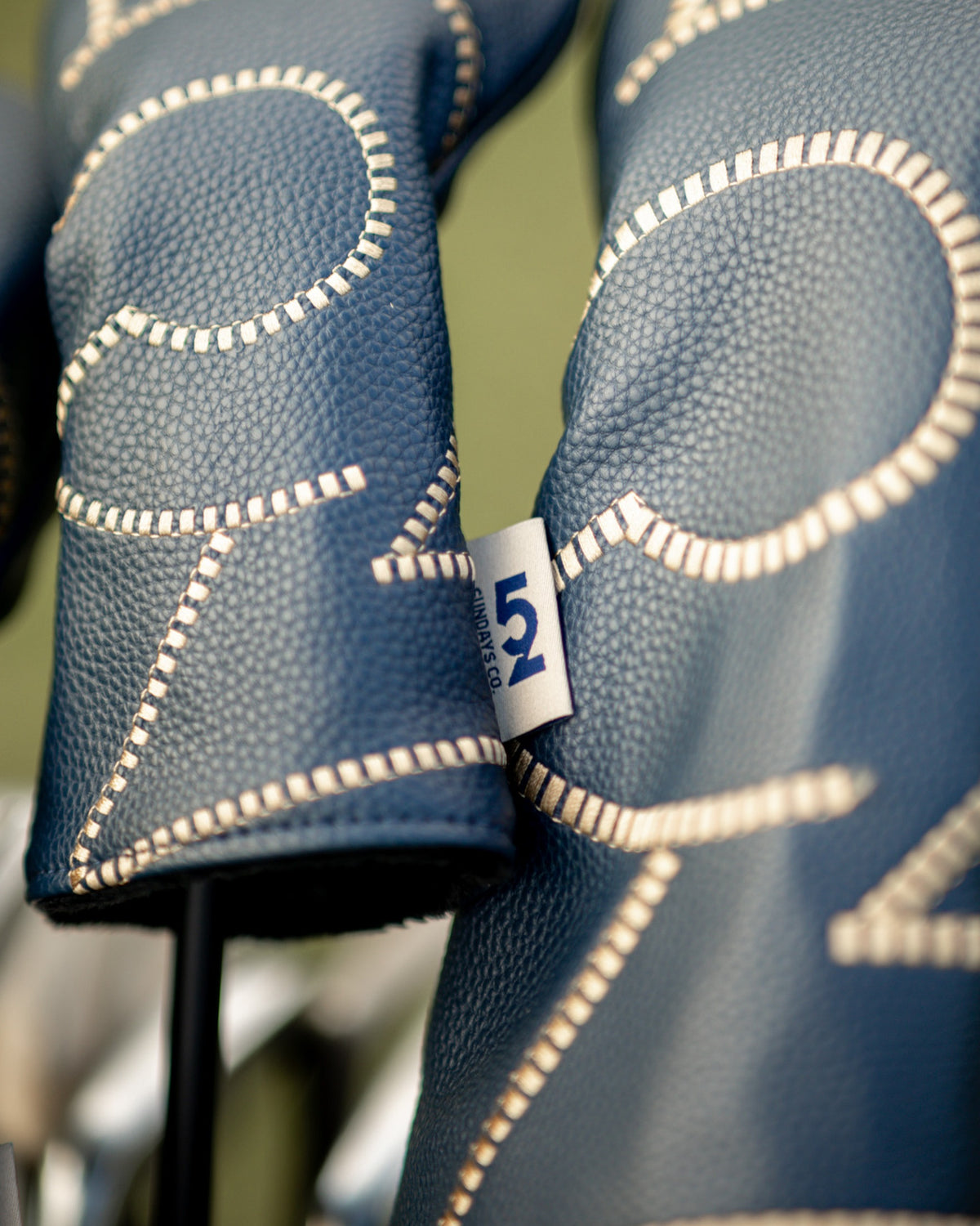 Close-up of the hand-stitched cream detailing and woven '52 Sundays Co.' tag on a 52 Sundays leather headcover