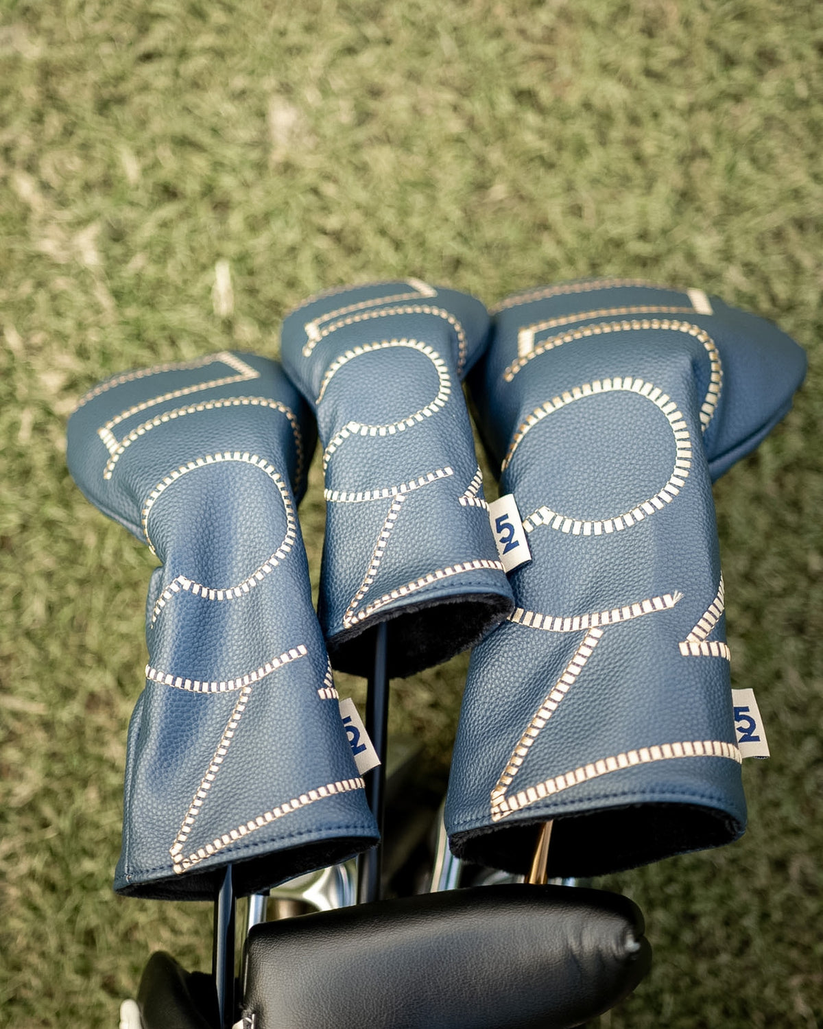 Set of three 52 Sundays navy leather headcovers with cream stitching and woven '52' tags, resting in a golf bag on the fairway