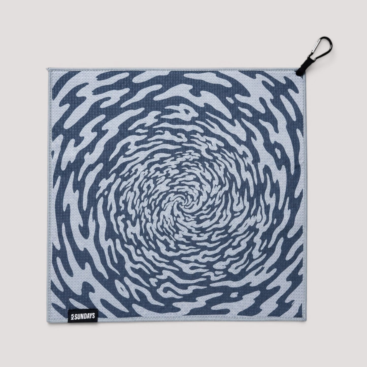 A square golf towel with a blue and white spiral pattern, featuring a black carabiner clip on the top right corner and a small black brand tag reading '52 SUNDAYS' in the bottom left corner, set against a solid light gray background.
