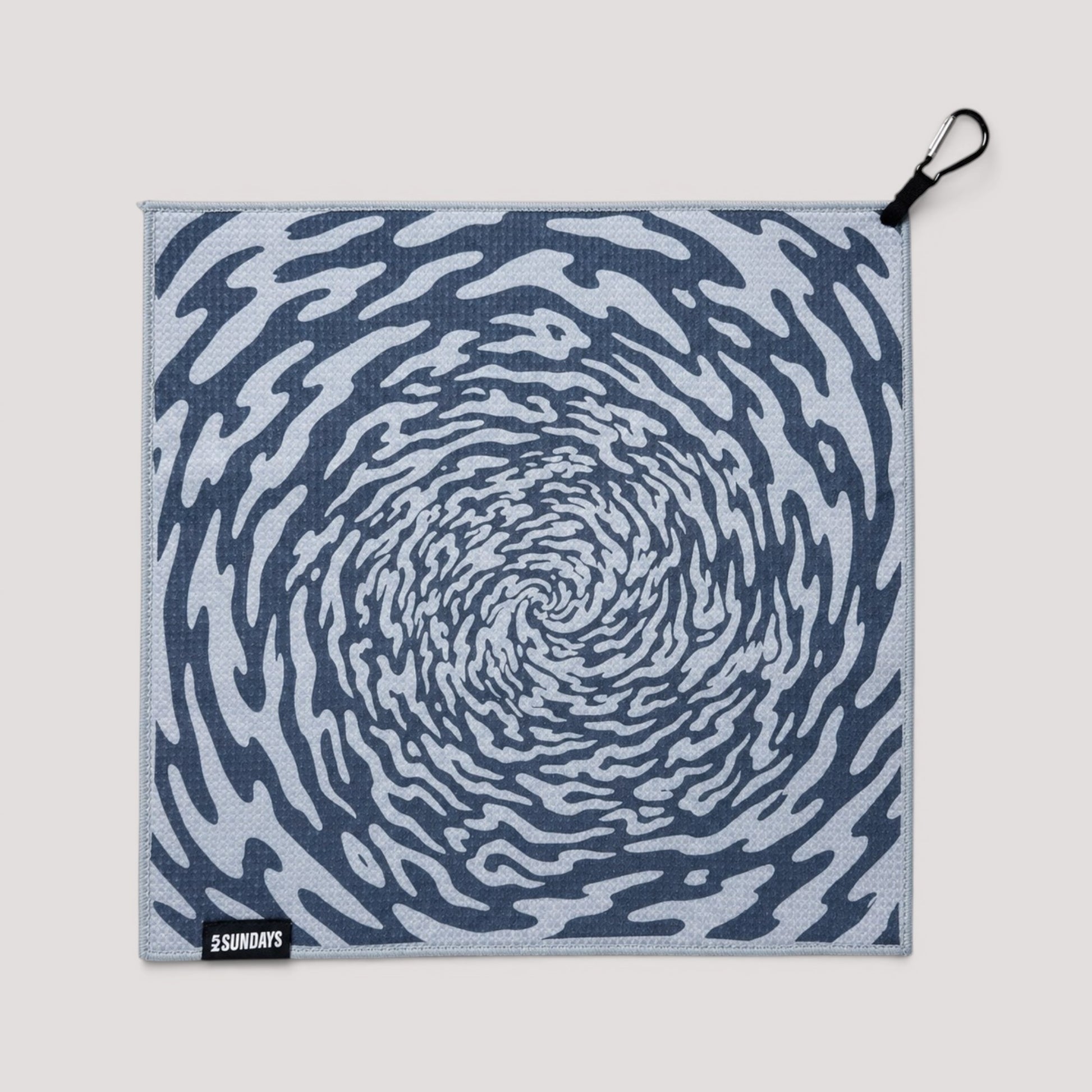 A square golf towel with a blue and white spiral pattern, featuring a black carabiner clip on the top right corner and a small black brand tag reading '52 SUNDAYS' in the bottom left corner, set against a solid light gray background.