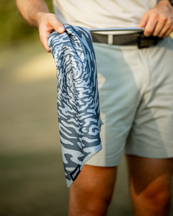A close-up of a person outdoors holding a blue and gray patterned golf towel, cleaning a golf club