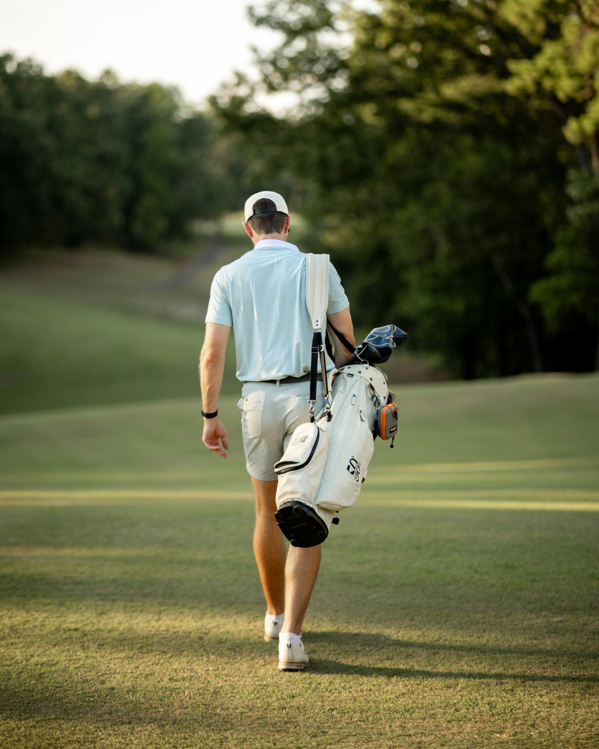 Back view of a golfer in the Hermosa Sage Polo walking down the fairway with a white stand bag.