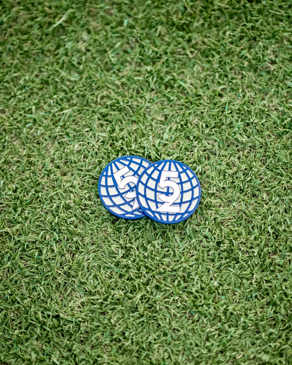 Two 52 Sundays navy globe-design golf ball markers resting on artificial turf, showing the '52' logo detail