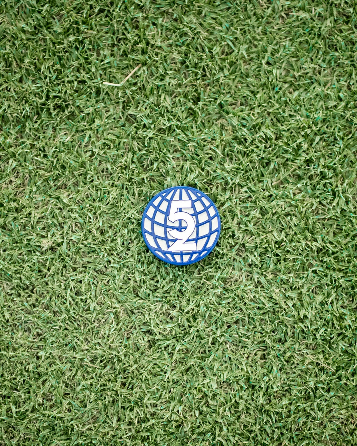 Close-up overhead shot of a single 52 Sundays globe ball marker on turf, showing the blue and white '52' logo design